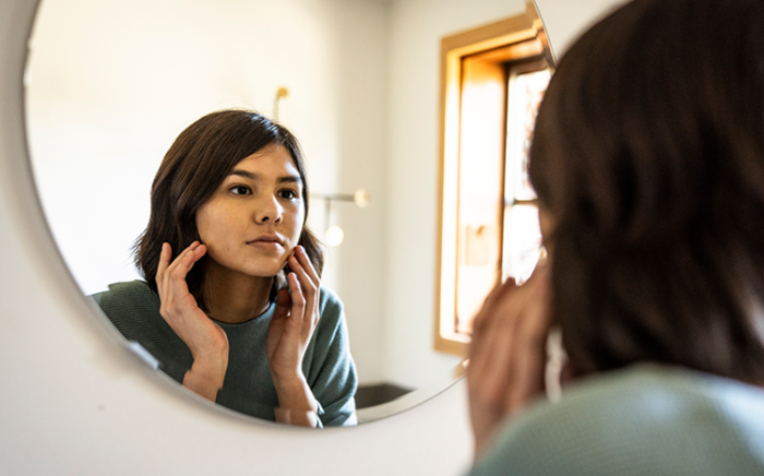 Woman looking at the mirror and feeling her face